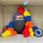 Race car-themed birthday decoration with colorful balloon garland and backdrop.