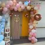 Elegant newborn arrival celebration -Balloon archway: Features a beautiful balloon archway in shades of pink- white- gold- and copper- creating a festive and celebratory entrance -Welcome sign: Includes a "Welcome Tala" sign with a golden frame- adding a personal and welcoming touch to the decoration -Sheer fabric backdrop: Features a sheer pink fabric backdrop behind the welcome sign- adding elegance and softness to the setup -Decorative boxes: Includes decorative boxes spelling out "Baby name"- adding a playful and personalized element -Additional balloon decorations: The arrangement has additional balloon decorations in coordinating colors- enhancing the celebratory atmosphere -Color Palette: The color palette is soft and elegant- perfect for welcoming a new baby.