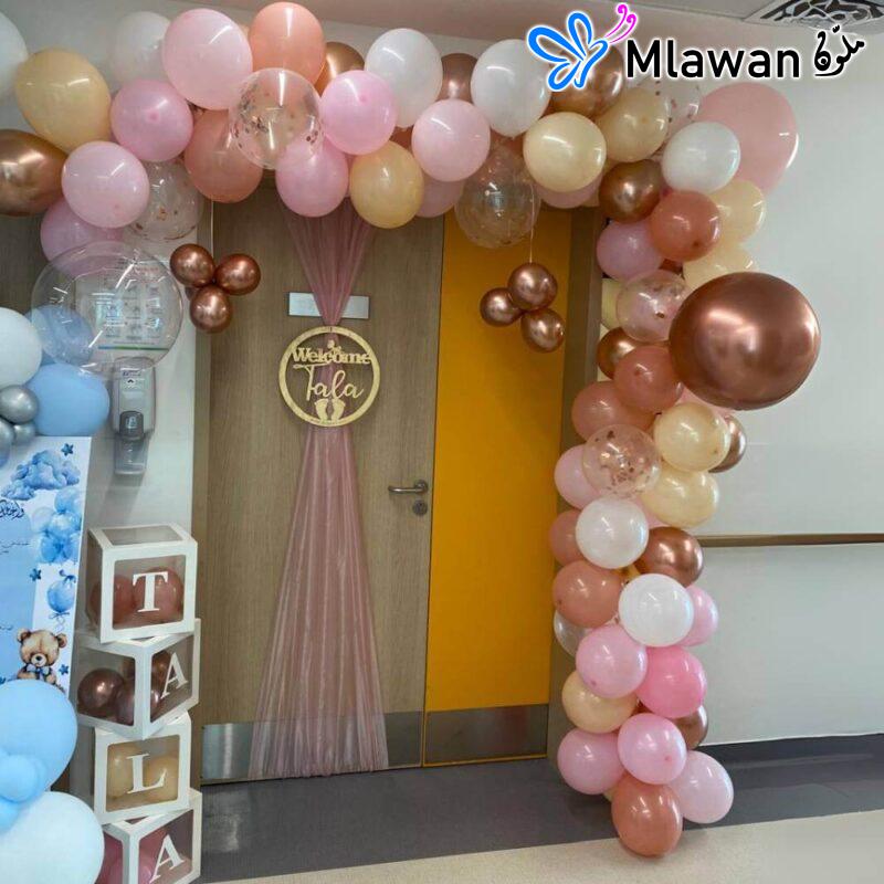 Elegant newborn arrival celebration -Balloon archway: Features a beautiful balloon archway in shades of pink- white- gold- and copper- creating a festive and celebratory entrance -Welcome sign: Includes a "Welcome Tala" sign with a golden frame- adding a personal and welcoming touch to the decoration -Sheer fabric backdrop: Features a sheer pink fabric backdrop behind the welcome sign- adding elegance and softness to the setup -Decorative boxes: Includes decorative boxes spelling out "Baby name"- adding a playful and personalized element -Additional balloon decorations: The arrangement has additional balloon decorations in coordinating colors- enhancing the celebratory atmosphere -Color Palette: The color palette is soft and elegant- perfect for welcoming a new baby.